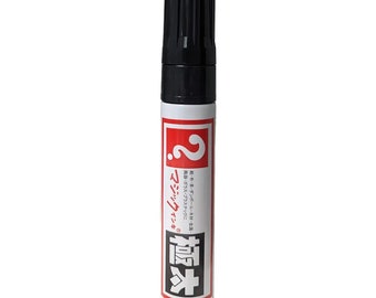May include: A white marker with a black cap. The marker has red text that says "マジックインキ" and "極" with a question mark in a red square. The text says "紙・布・革・ダンボール・木材・金属・陶器・ガラス・プラスチックに".