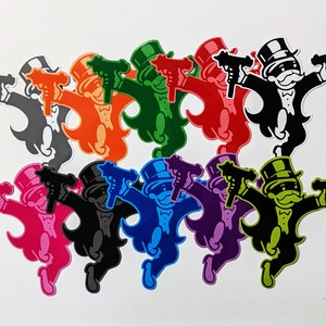 May include: A collection of colorful Monopoly Man character cutouts, each holding two toy guns. The characters are in various colors, including black, gray, orange, green, red, pink, blue, purple, and yellow, all against a white background.