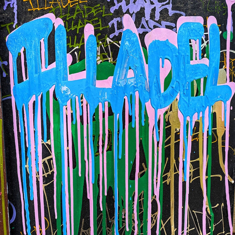 May include: A close-up of the word "LADEL" painted in blue and pink on a black surface. The paint is dripping down the surface, creating a colourful and abstract design.