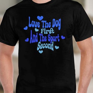 May include: Black t-shirt with the text "Love The Dog First And The Sport Second" in blue script. The text is decorated with small blue hearts. The shirt is a crew neck style.