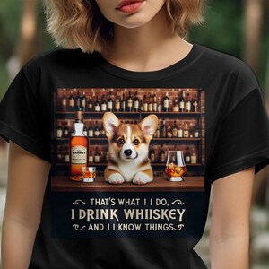 May include: A black t-shirt with a graphic of a corgi dog sitting at a bar with a glass of whiskey. The text on the shirt reads "That's what I do, I drink whiskey and I know things."