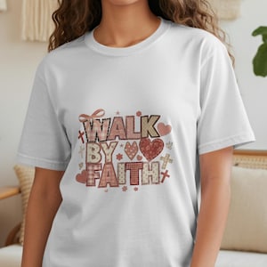 Może przedstawiać: Biała koszulka z napisem "WALK BY FAITH" w dekoracyjnym wzorze. Wzór zawiera serca, krzyże i wzory w kratę w odcieniach czerwieni, różu i brązu. Koszulka ma krótkie rękawy i okrągły dekolt.