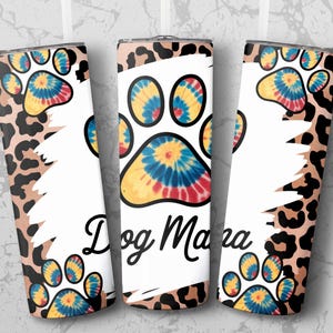 May include: A set of three stainless steel tumblers with a white background and a leopard print pattern. Each tumbler features a tie-dye paw print design and the words "Dog Mama" in black script.