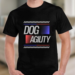 May include: Black t-shirt with the words "DOG AGILITY" in white, with a red and blue gradient design. The shirt has a checkered pattern above and below the text.