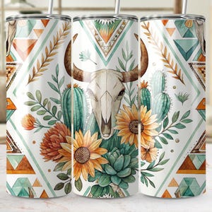 May include: A white tumbler with a Southwestern design featuring a bull skull, sunflowers, cacti, and geometric patterns in shades of orange, teal, and brown. The tumbler has a straw and is approximately 20 cm tall.