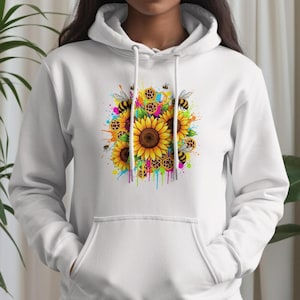 May include: White hoodie featuring a colorful graphic of sunflowers and bees. The design includes yellow sunflowers, buzzing bees, and a vibrant splash of paint in various colors. The hoodie has a drawstring hood and a front pocket.