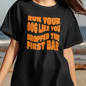 May include: Black t-shirt with orange text that reads "Run your dog like you dropped the first bar".