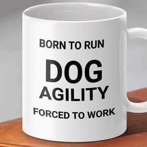 Op de afbeelding: Witte keramische mok met zwarte tekst die "Born to Run Dog Agility Forced to Work" luidt.