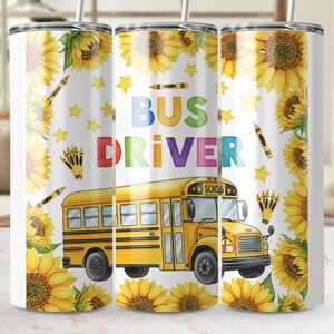 Puede incluir: Un vaso blanco con un diseño que presenta un autobús escolar amarillo y las palabras "BUS DRIVER" en colores brillantes. El diseño también incluye girasoles, estrellas y crayones. Un regalo atento para un conductor de autobús.