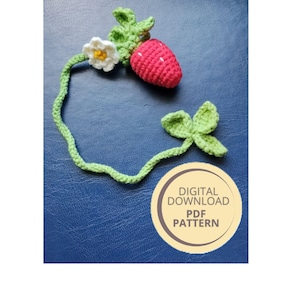 May include: Crocheted strawberry with green leaves and a white flower. The strawberry is red with a textured surface. The stem is green and connects to a leaf and a flower. The image includes text that says "DIGITAL DOWNLOAD PDF PATTERN."