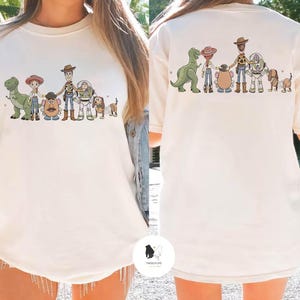 Peut inclure: T-shirt cr&egrave;me avec une illustration de personnages de dessin anim&eacute; populaire. L'avant et l'arri&egrave;re du t-shirt pr&eacute;sentent le m&ecirc;me motif. Le t-shirt a des manches courtes et un col rond.