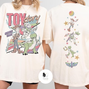 May include: Cream-colored t-shirt featuring a Toy Story graphic. The front displays Woody, Buzz Lightyear, and Rex with the text "TOY STORY SINCE 1995". The back shows various characters and elements from the movie. A fun, nostalgic design.