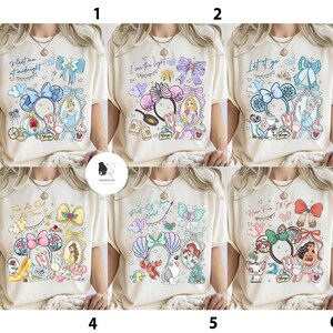 May include: Six cream-colored t-shirts with different Disney-themed designs. Each shirt features a character portrait, a bow, and text like "Meet me at midnight" or "Let it go." The designs include Cinderella, Rapunzel, Elsa, Belle, Ariel, and Moana.