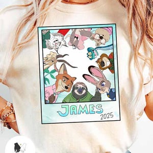 以下が含まれることがあります： ズートピアのキャラクターの漫画のイメージがプリントされたクリーム色のTシャツ。 画像はポラロイドのようにフレームされており、「JAMES」という名前と「2025」という年が水色のフォントで表示されています。 Tシャツは丸いネックラインと半袖です。