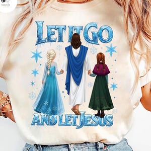 May include: Cream-colored t-shirt featuring the text "LET IT GO AND LET JESUS" in blue. The graphic depicts Jesus holding hands with two cartoon characters in blue and green dresses, with snowflakes.