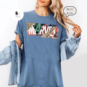 Op de afbeelding: Een blauw t-shirt met het Marvel-logo in een kleurrijk, geometrisch ontwerp. Het shirt bevat de woorden "Iron Man", "Captain America", "Black Widow" en "Avengers". Het t-shirt is een casual stijl.