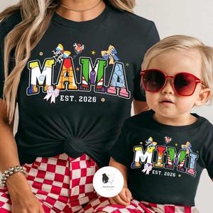 May include: Black t-shirts featuring the words "MAMA" and "MIMI" in vibrant colours, with "EST. 2026" beneath. The "MAMA" shirt is paired with red and white checked shorts. The child wearing the "MIMI" shirt has red sunglasses.
