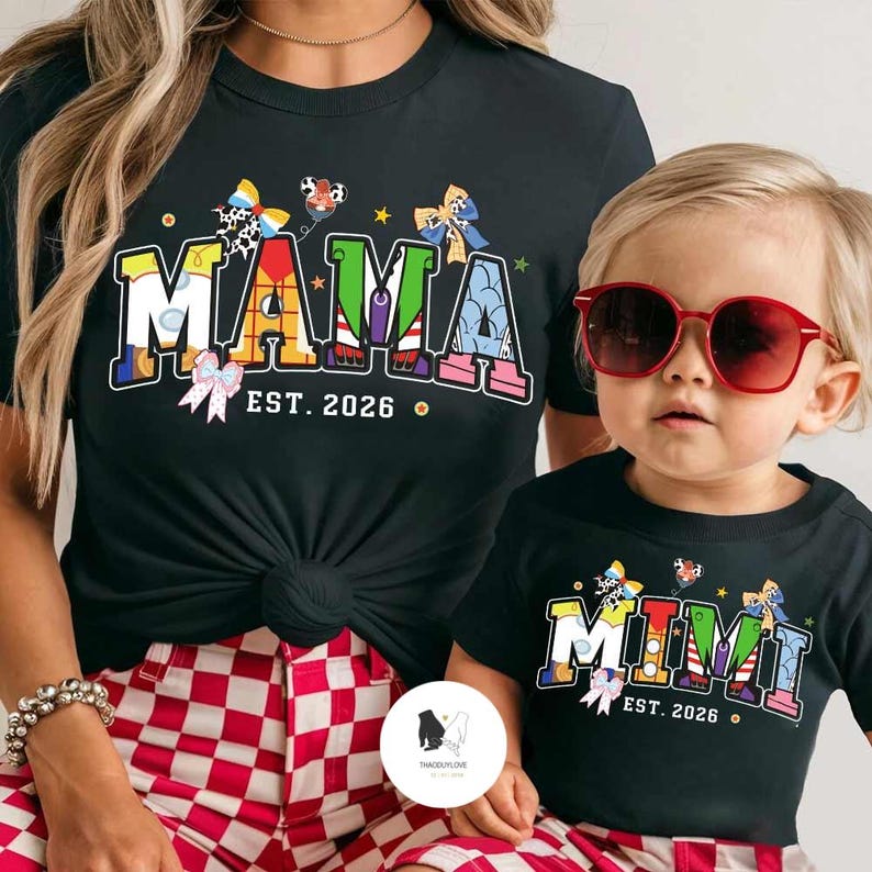 May include: Black t-shirts featuring the words "MAMA" and "MIMI" in vibrant colours, with "EST. 2026" beneath. The "MAMA" shirt is paired with red and white checked shorts. The child wearing the "MIMI" shirt has red sunglasses.