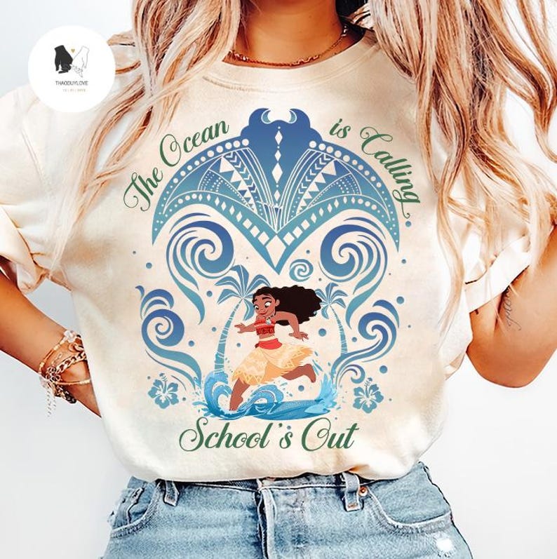 Op de afbeelding: Een cr&egrave;mekleurig T-shirt met een afbeelding van een stripfiguur die op een strand met palmbomen en oceaangolven rent. Het ontwerp bevat blauwe tribale patronen en de groene tekst "The Ocean is Calling" en "School's Out" in een sierlijk lettertype.
