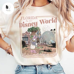 Puede incluir: Camiseta color crema con un gr&aacute;fico retro de Disney World en Florida. El dise&ntilde;o incluye las palabras "Florida Disney World Est. 1971" y un dibujo animado de Daisy Duck. Tambi&eacute;n se incluye la frase "The happiest place on earth".