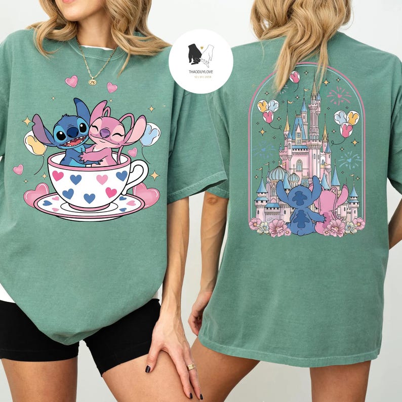 May include: Green t-shirt featuring a cartoon design of Stitch and Angel in a teacup with hearts and balloons. The back of the shirt shows a castle with Stitch and Angel. The shirt has short sleeves.