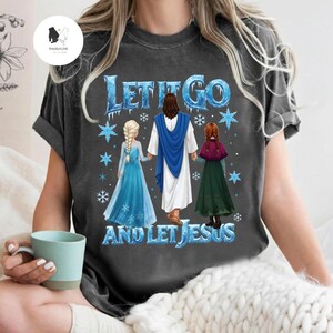 May include: Dark gray t-shirt with the text "LET IT GO AND LET JESUS" in blue and white. The graphic features Jesus holding hands with two cartoon characters in blue and green dresses, with snowflakes.