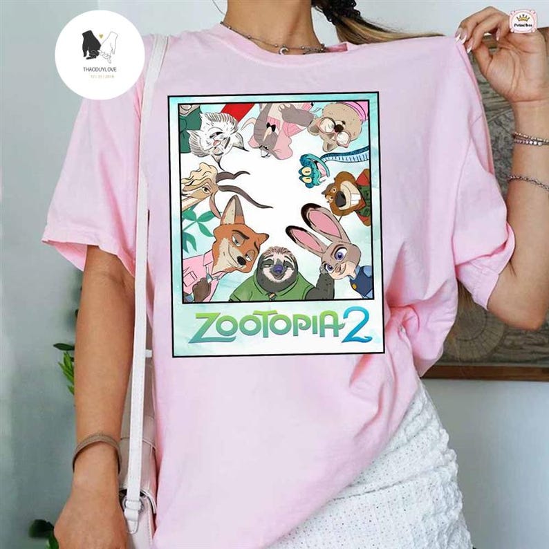 以下が含まれることがあります： アニメ映画「ズートピア2」のキャラクターが描かれた、明るいピンク色のTシャツ。 グラフィックは黒い枠で囲まれ、映画のタイトルが緑と青で表示されています。 シャツは柔らかい素材で作られています。
