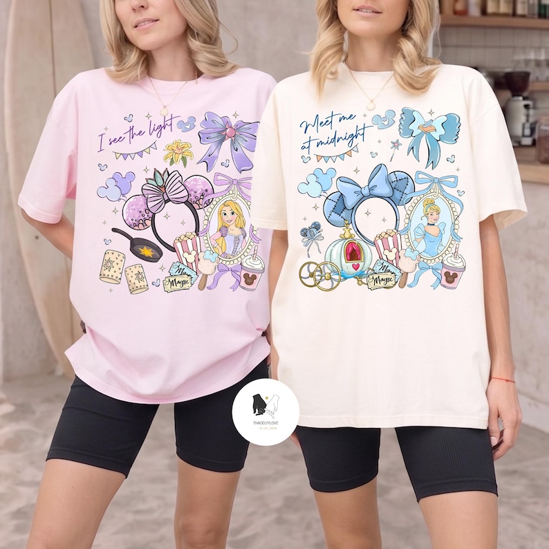 May include: Two t-shirts, one pink and one cream, featuring Disney-themed graphics. The pink shirt has the text "I see the light" and a Rapunzel design. The cream shirt says "Meet me at midnight" with a Cinderella design. Both shirts have black shorts.