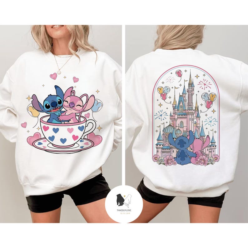 May include: White sweatshirt featuring a cartoon illustration of Stitch and Angel hugging in a teacup with hearts. The back of the sweatshirt shows Stitch and Angel in front of a castle with fireworks and balloons. The brand name is at the bottom.