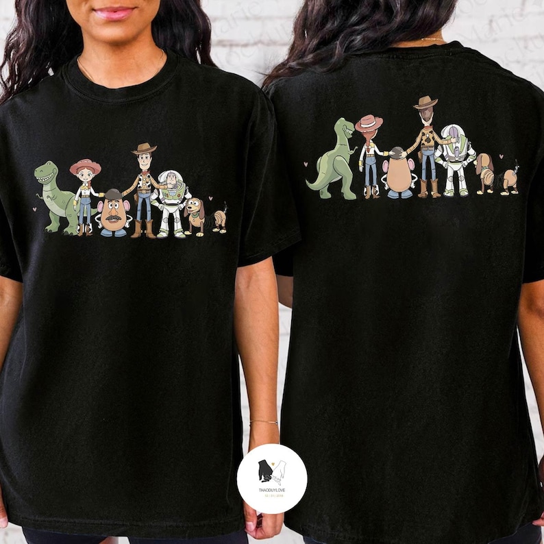 Peut inclure: T-shirts noirs avec une illustration de dessin anim&eacute; de personnages d'un film d'animation populaire. Le design comprend un dinosaure vert, une cowgirl, un cow-boy, une t&ecirc;te de pomme de terre, un ranger de l'espace, un chien et un petit chien.