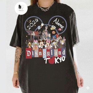 May include: Black t-shirt featuring a Disneyland Tokyo design with Mickey and Minnie Mouse, Donald Duck, and other Disney characters. The design includes the text "2026" and "Name" within Mickey Mouse ears, and the words "Disneyland Tokyo".