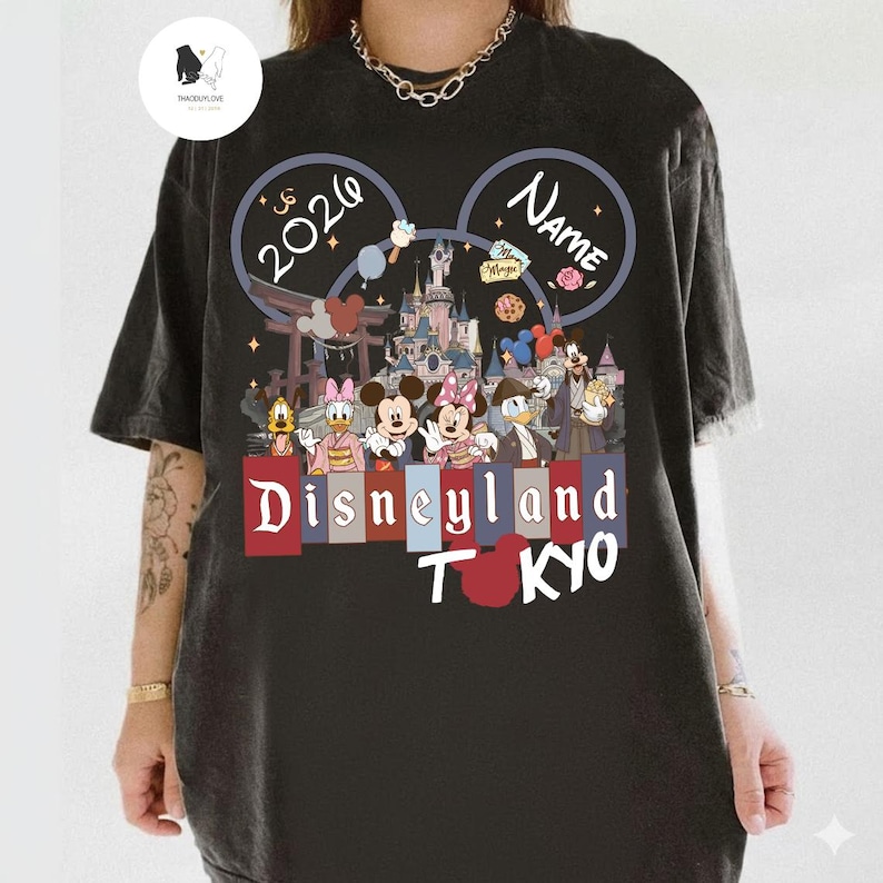 May include: Black t-shirt featuring a Disneyland Tokyo design with Mickey and Minnie Mouse, Donald Duck, and other Disney characters. The design includes the text "2026" and "Name" within Mickey Mouse ears, and the words "Disneyland Tokyo".