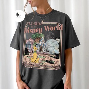 Puede incluir: Camiseta gris oscuro con un gr&aacute;fico de estilo vintage de Florida Disney World. El dise&ntilde;o incluye a Pluto, el castillo de Cenicienta y Spaceship Earth, con el texto "Florida Disney World" y "The happiest place on earth."