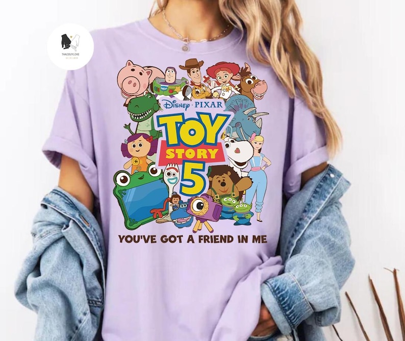 May include: A lilac t-shirt with a vibrant graphic of characters from the Disney Pixar film Toy Story 5. The design includes the film's title and the words "You've Got a Friend in Me".