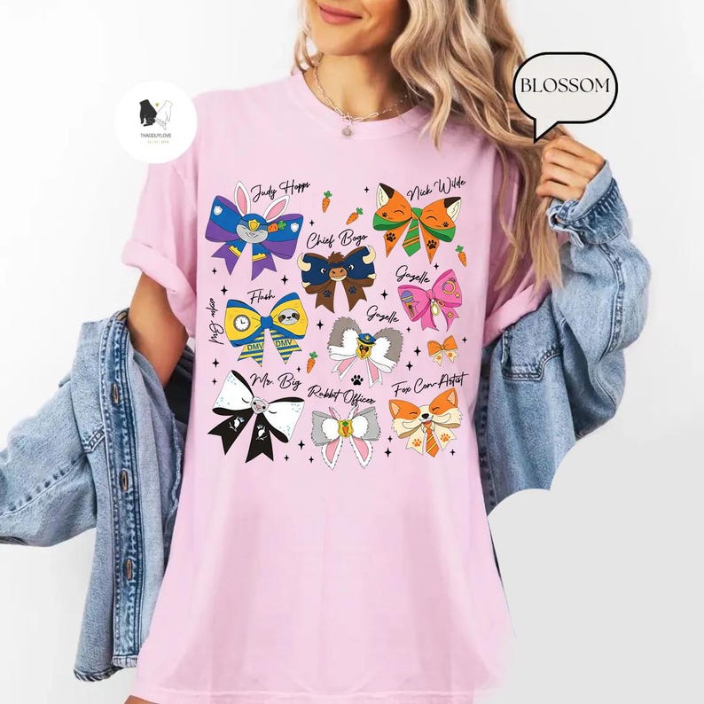Puede incluir: Una camiseta rosa claro con dise&ntilde;os de lazos coloridos y nombres de personajes como "Judy Hoppe" y "Nick Wilde". Los lazos tienen varios patrones y colores, incluyendo azul, verde y naranja. La palabra "BLOSSOM" est&aacute; en una burbuja.
