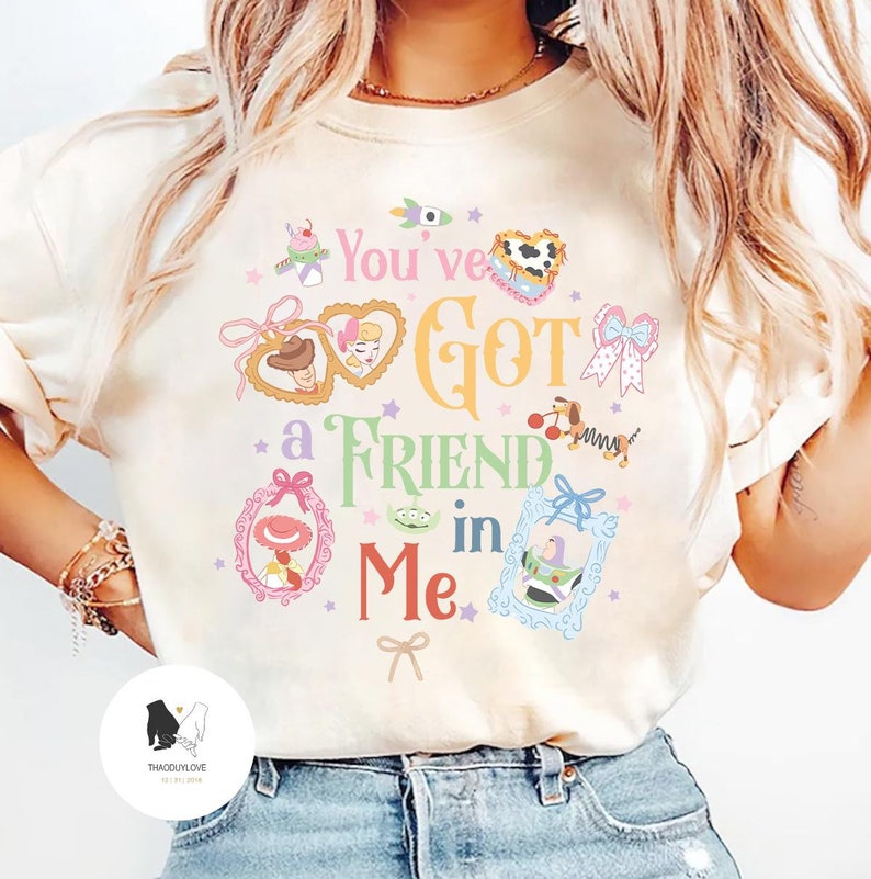 May include: Cream-colored sweatshirt featuring the phrase "You've Got a Friend in Me" in colorful, whimsical lettering. The design includes various cartoon character illustrations within decorative frames and star accents.
