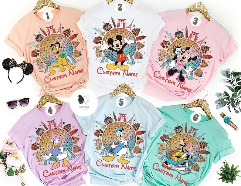 May include: Six colorful t-shirts featuring Disney characters and a globe design with landmarks. Each shirt has a different character: Pluto, Mickey Mouse, Minnie Mouse, Daisy Duck, Donald Duck, and Goofy. The text "Custom Name" is printed on each shirt.