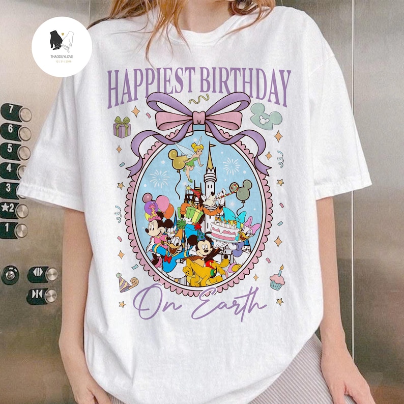 May include: White t-shirt with a colorful graphic featuring Disney characters and the text "Happiest Birthday On Earth." The design includes Mickey Mouse, Minnie Mouse, Donald Duck, and other characters, with a castle and fireworks.