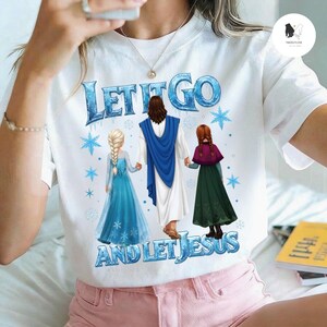 May include: White t-shirt with the text "LET IT GO AND LET JESUS" in blue. The graphic features Jesus holding hands with two cartoon characters in blue and green dresses. Blue snowflakes are scattered around the text.