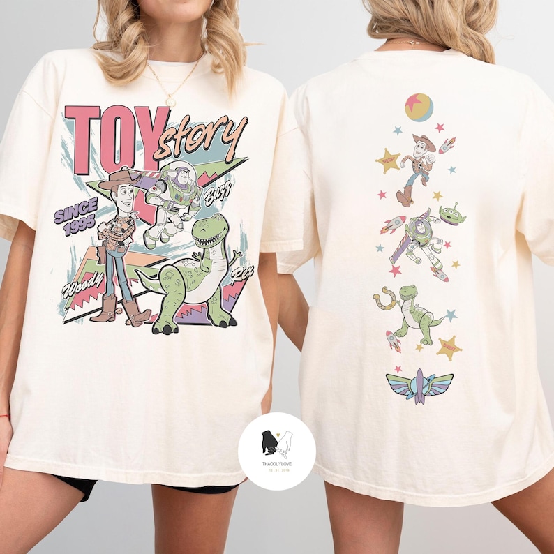 May include: Cream-colored t-shirt featuring a Toy Story graphic. The front displays Woody, Buzz Lightyear, and Rex with the text "TOY STORY SINCE 1995". The back shows various characters and elements from the movie. A fun, nostalgic design.