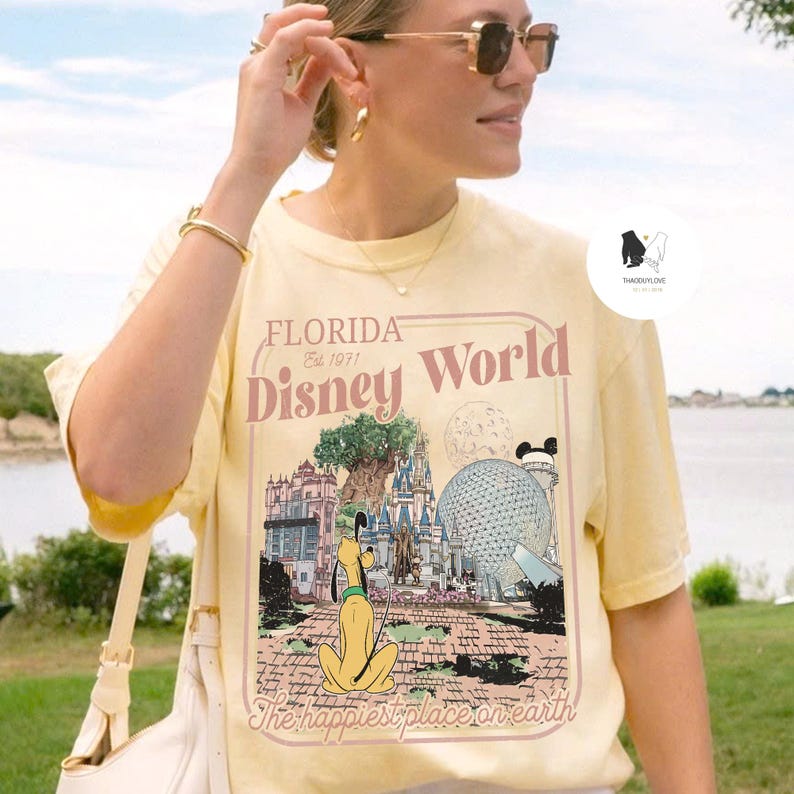 Puede incluir: Camiseta amarilla clara con un gr&aacute;fico de Florida Disney World, con Pluto. El texto en la camiseta dice "Florida Disney World Est. 1971" y "The happiest place on earth."