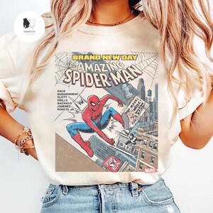 Puede incluir: Camiseta color crema con un gr&aacute;fico de c&oacute;mic de Spider-Man en acci&oacute;n. El dise&ntilde;o incluye el texto "BRAND NEW DAY" y "The AMAZING SPIDER-MAN", junto con los nombres de los creadores del c&oacute;mic y el logo de Marvel.