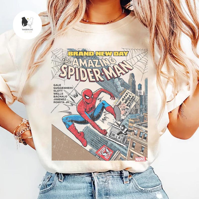 Puede incluir: Camiseta color crema con un gr&aacute;fico de c&oacute;mic de Spider-Man en acci&oacute;n. El dise&ntilde;o incluye el texto "BRAND NEW DAY" y "The AMAZING SPIDER-MAN", junto con los nombres de los creadores del c&oacute;mic y el logo de Marvel.