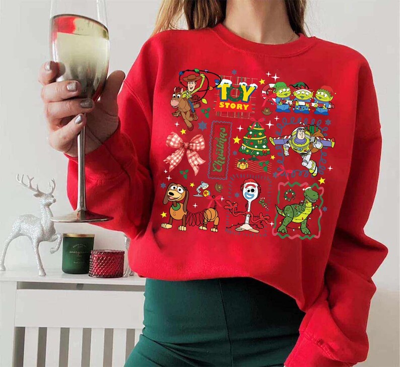 May include: Red sweatshirt featuring a colorful Toy Story Christmas design. The graphic includes Woody, Buzz Lightyear, and other characters, along with a Christmas tree and the words "Toy Story Christmas".