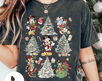 May include: Dark gray t-shirt featuring a festive Christmas design. The design includes images of Mickey Mouse, Donald Duck, and Goofy, each adorned with holiday lights and surrounded by Christmas trees and gifts. A Santa hat and candy cane are also included.