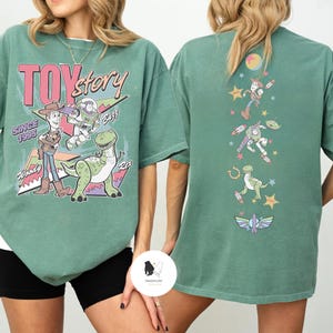 May include: Green t-shirt featuring Toy Story characters Woody, Buzz Lightyear, and Rex, with the text "Toy Story Since 1995" on the front. The back of the shirt displays additional characters and graphics.