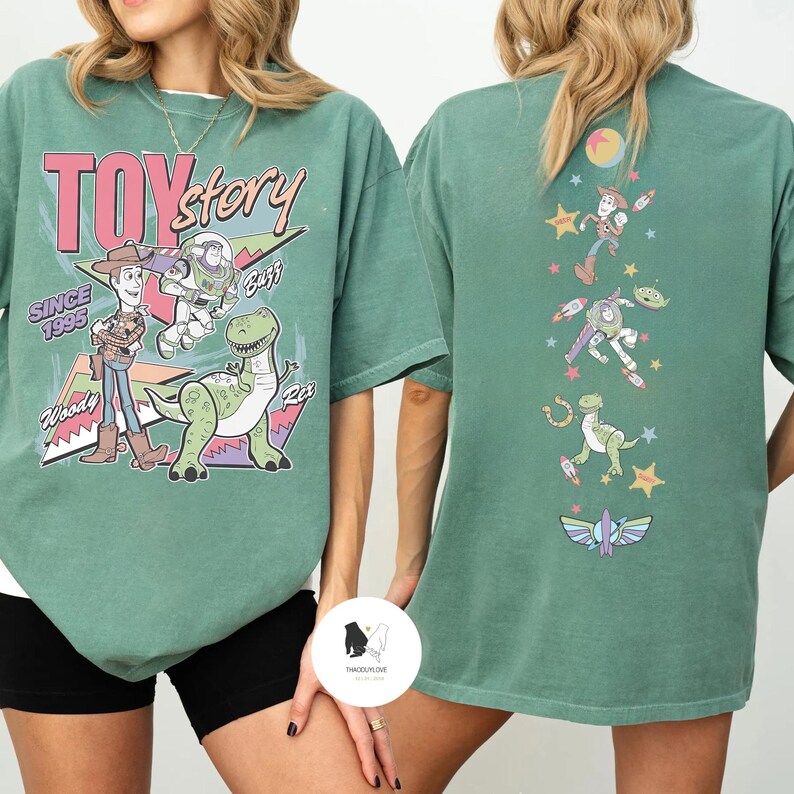 May include: Green t-shirt featuring Toy Story characters Woody, Buzz Lightyear, and Rex, with the text "Toy Story Since 1995" on the front. The back of the shirt displays additional characters and graphics.