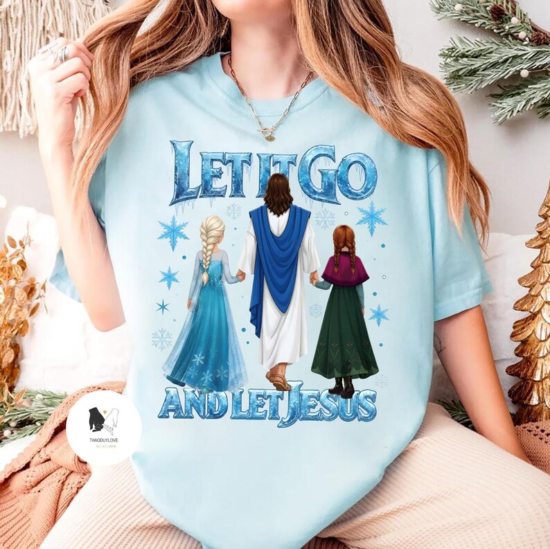 May include: Light blue t-shirt with the text "LET IT GO AND LET JESUS". The graphic features three figures: two girls in dresses and a figure in a white robe and blue shawl. Snowflakes are also included in the design.