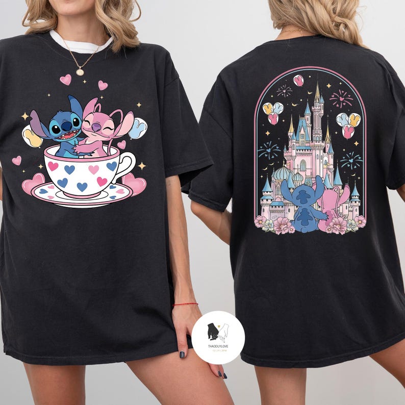 May include: Black t-shirt featuring a cartoon design of Stitch and Angel. The front shows them in a teacup with hearts, while the back displays a castle scene with fireworks and balloons. A cute and colorful design.