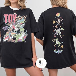 May include: Black t-shirt featuring a colorful graphic of Toy Story characters, including Woody, Buzz Lightyear, and Rex, with the text "TOY STORY" and "SINCE 1995". The back of the shirt displays additional character illustrations.